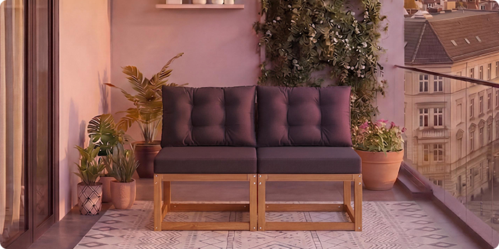 Dvousedadlová modulární dřevěná pohovka s tmavě šedými polštáři na balkóně obklopeném hrnkovými rostlinami a výhledem na město v pozadí